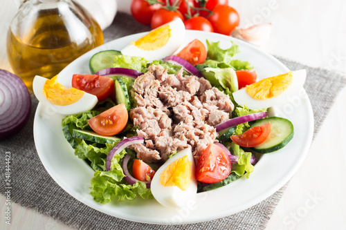 Fresh fish tuna salad made of tomato, ruccola, tuna, eggs, arugula, crackers and spices. Caesar salad in a white bowl on wooden background