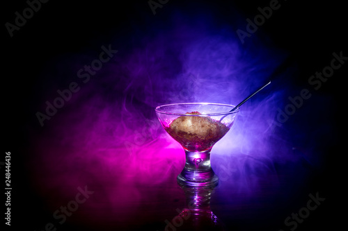 Glass filled with colorful fruit ice cream on dark background with toned light and fog