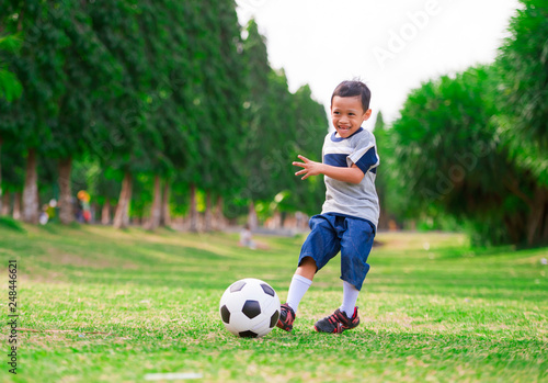 lifestyle portrait at grass city park of 5 years old Asian Indonesian kid playing football happy and excited kicking the ball smiling cheerful in child sport practice education