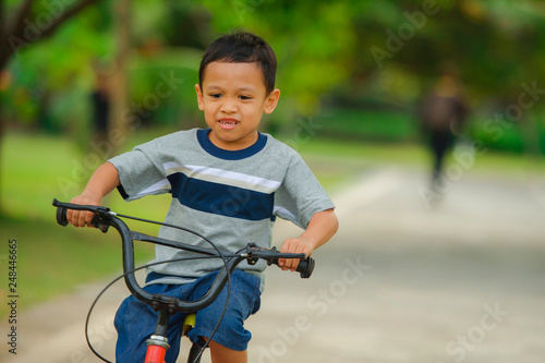 lifestyle portrait of young happy and excited 5 years old Asian Indonesian child enjoying learning bike at city park isolated on trees background in kid having fun