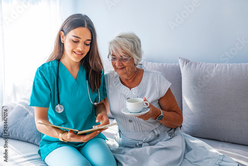 Young caregiver and senior woman laughing together while sitting on sofa photo