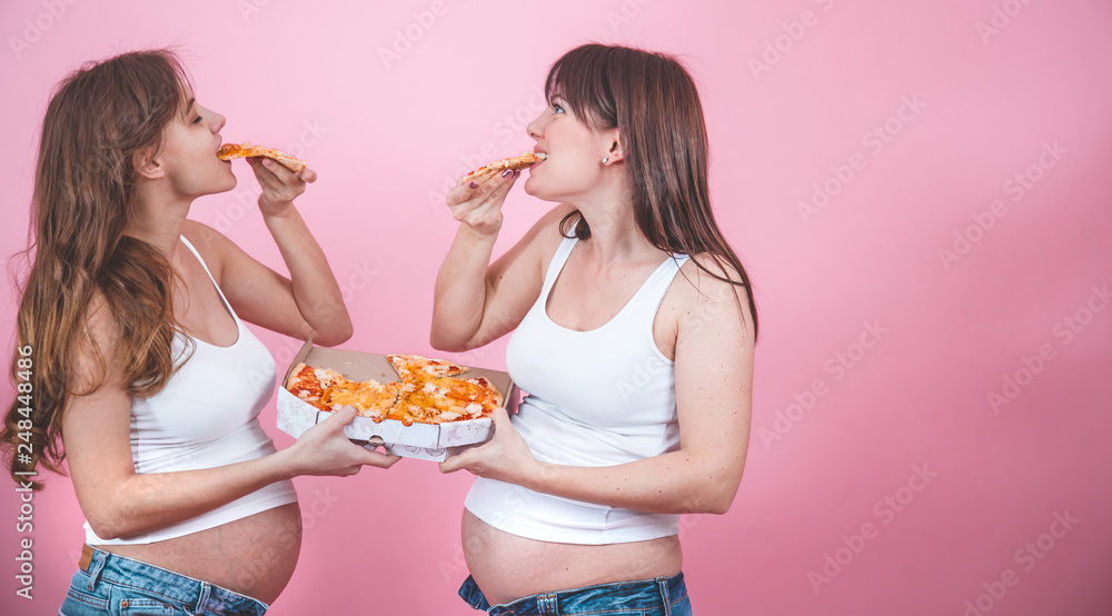nutrition concept, pregnant women eating pizza on a pink background nutrition concept, pregnant women eating pizza on a pink background