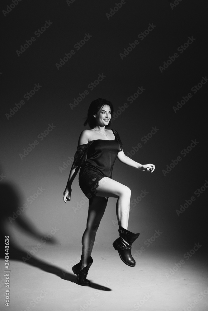 Fashion Full Length portrait. Young positive brunette lady in stylish black dress posing on dark background. Shadows on the wall Fashion Full Length portrait. Young positive brunette lady in stylish black dress posing on dark background. Shadows on the wall