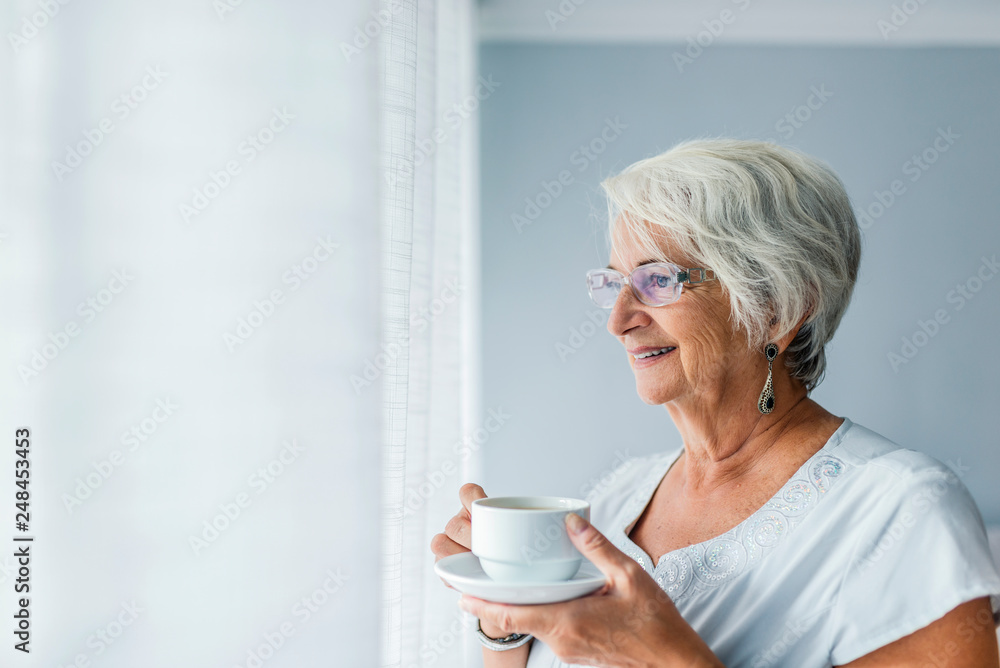 Senior woman at the window holding a cup of tea Senior woman at the window holding a cup of tea