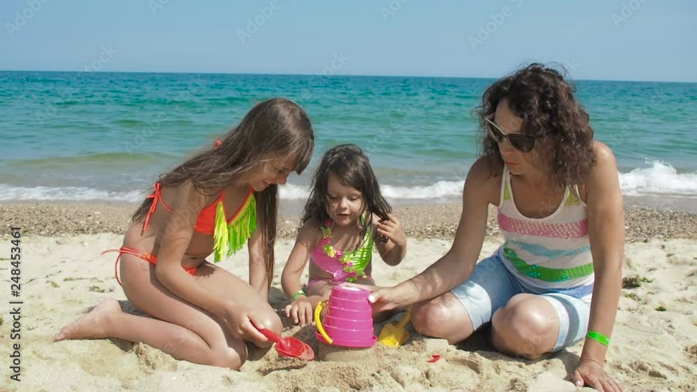 Mother playing with daughters on sand. Family on the beach playing with sand. Children together with their mother are building a castle from the sand. Mother playing with daughters on sand. Family on the beach playing with sand. Children together with their mother are building a castle from the sand.