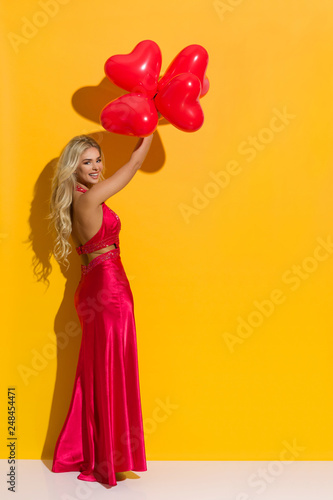 Beautiful Woman In Elegant Red Dress Is Holding Heart Shaped Balloons Over Her Head And Laughing © studioloco