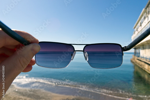 A man puts on sunglasses while standing on the seashore. First-person view