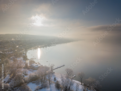 Aerial view of sunlight reflection on lake surface on cold winter morning. Fog over water, beautiful and tranquil scenery.