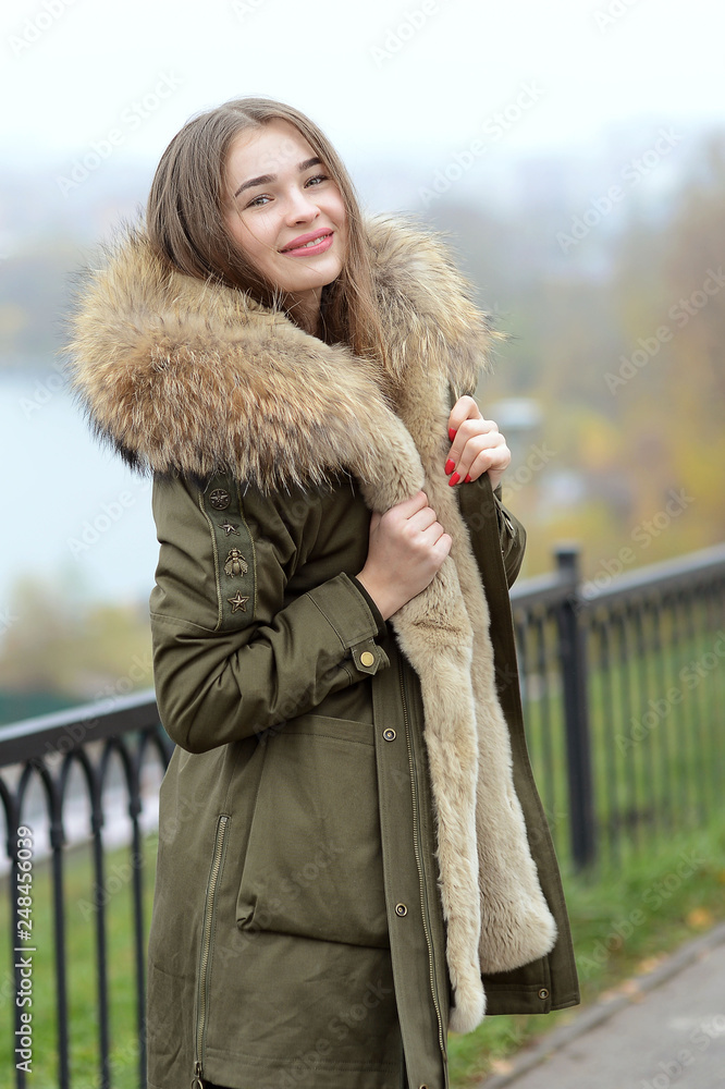a girl in a green jacket with a fur collar in glasses posing near the lake a girl in a green jacket with a fur collar in glasses posing near the lake