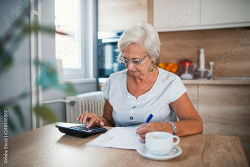 Serious elderly woman with calculator sitting at table