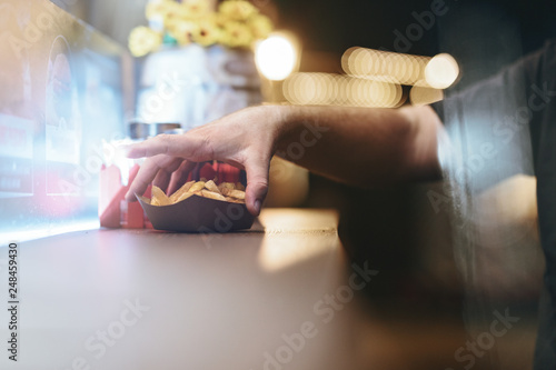 close up of man's hand tasting cheesy jalapeno skillet potatoes fries with cheddar and jalapenos from the food truck table at the street food festival in summer night light