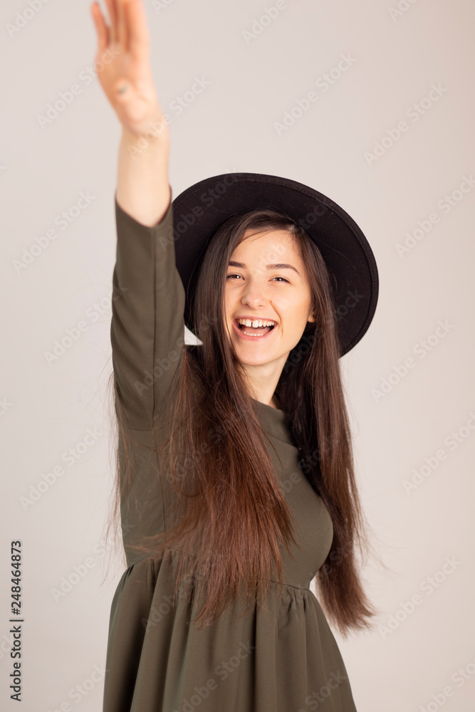 Young sensual caucasian woman in dark green (olive) dress holding fedora hat isolated on white-grey background with beautifull smile Young sensual caucasian woman in dark green (olive) dress holding fedora hat isolated on white-grey background with beautifull smile