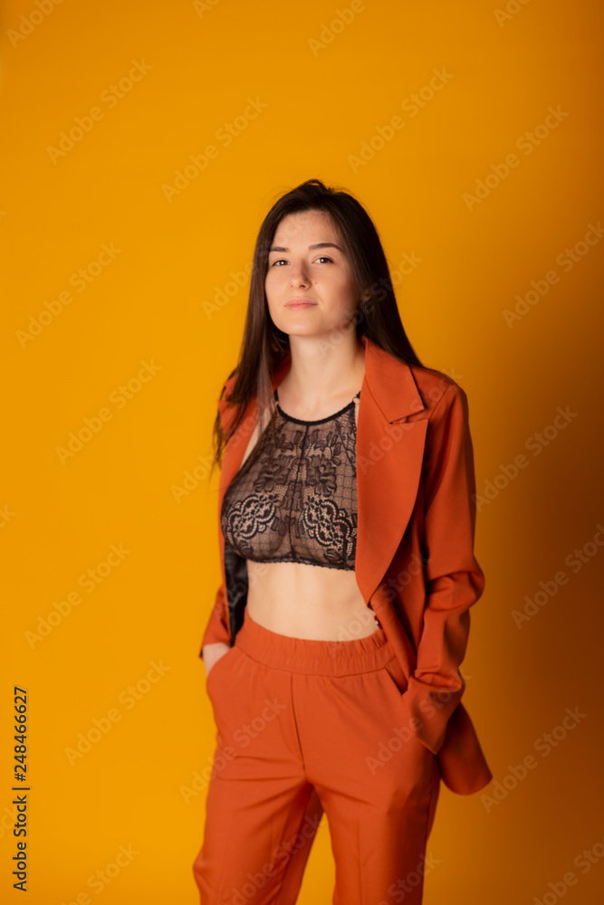sexy business lady dressed in a terracotta business suit with a jacket and trousers, under the jacket is seen a lively brassiere. Yellow background, bright colors sexy business lady dressed in a terracotta business suit with a jacket and trousers, under the jacket is seen a lively brassiere. Yellow background, bright colors