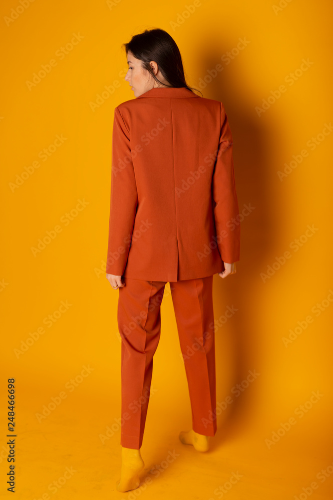 sexy business lady dressed in a terracotta business suit with a jacket and trousers. Yellow background, bright colors,rear view, minimalist design, space for your advertising sexy business lady dressed in a terracotta business suit with a jacket and trousers. Yellow background, bright colors,rear view, minimalist design, space for your advertising