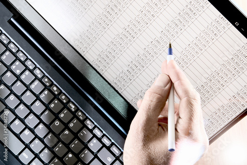 Hand with pen pointing at spreadsheet displayed on a laptop photo