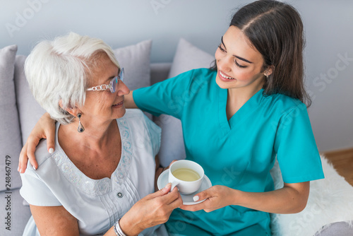 Young caregiver in uniform hugging smiling elderly woman during a home visit
