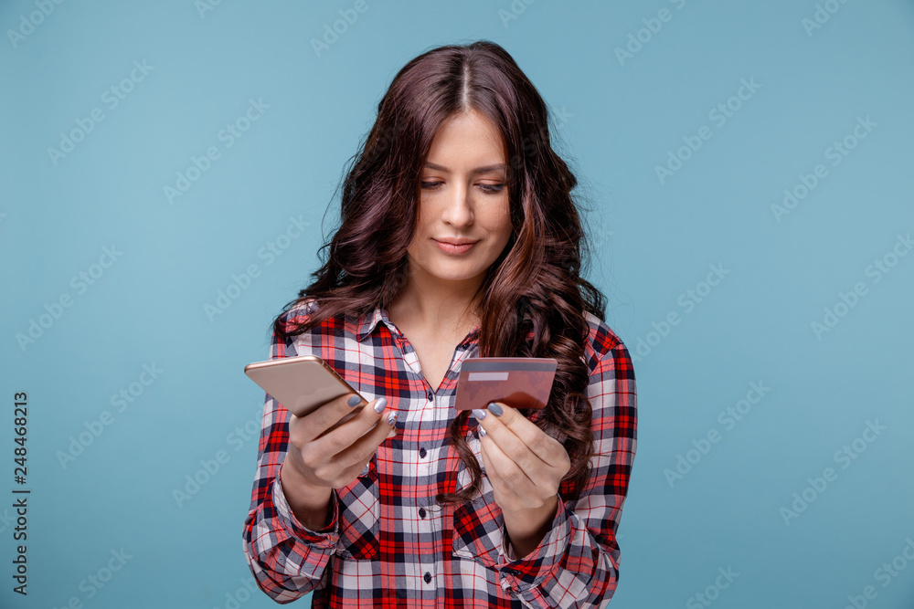young girl isolated over blue background using mobile phone holding credit card. young girl isolated over blue background using mobile phone holding credit card.