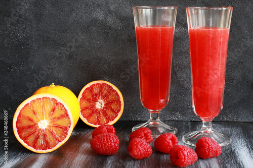 Orange juice, blood orange and raspberries on dark board