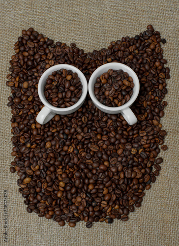 Owl made from coffee beans. Whole bean coffee. Coffee beans in the shape of an owl. Coffee cup on coffee beans. Coffee beans on burlap © Євген Малюга