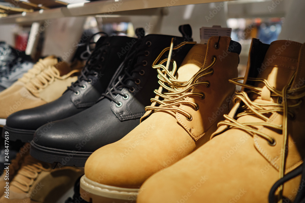 Row of contemporary stylish boots of brown and black colors arranged on shelf in clothes store