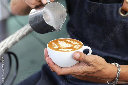 Barista pouring milk foam for making coffee latte art with pattern the leaves in a cup