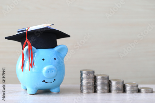 Wall Mural Graduation hat on blue piggy bank with stack of coins money on wooden background