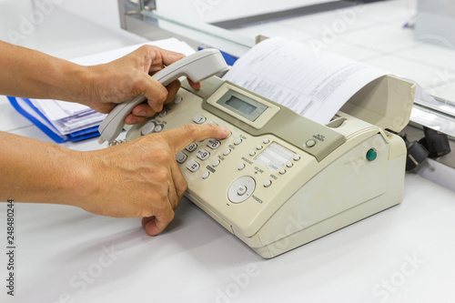 Hand man are using a fax machine send paper in the office Business concept  photo
