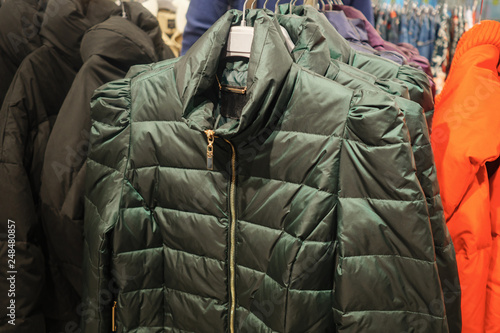 Rack with trendy warm coats of green color in clothes shop, close up