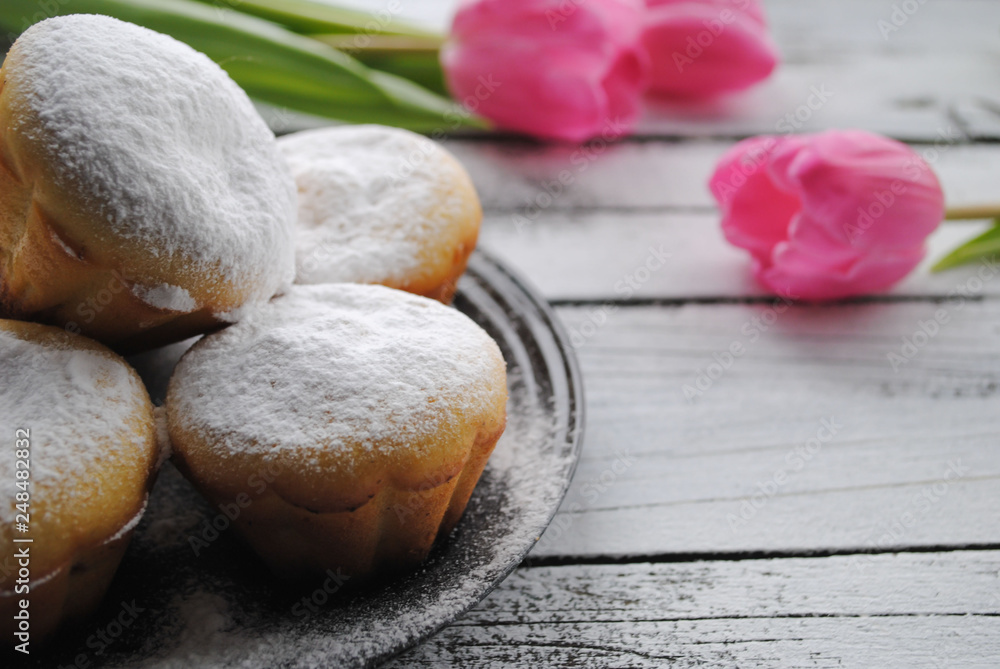 Cupcakes sprinkled with powdered sugar and pink tulips on a white table Cupcakes sprinkled with powdered sugar and pink tulips on a white table