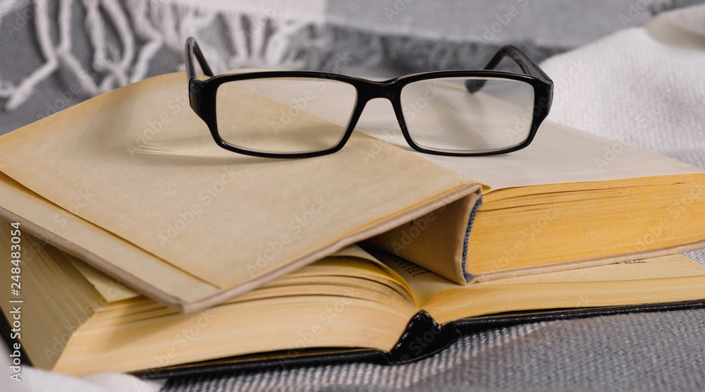Stack of open vintage books with glasses