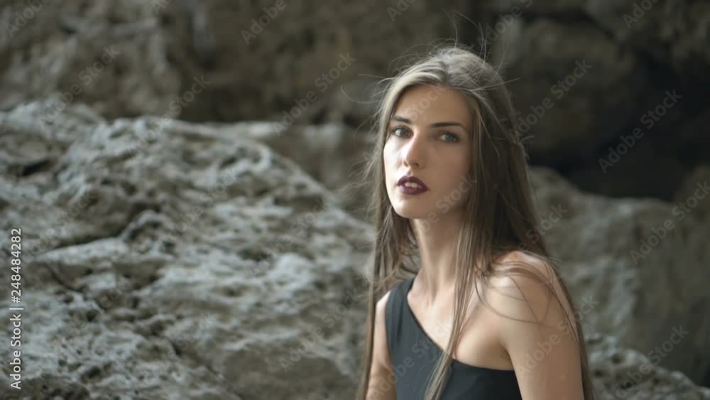 wonderful close view beautiful long haired woman with burgundy lipstick in black dress sits against bare rocks wonderful close view beautiful long haired woman with burgundy lipstick in black dress sits against bare rocks