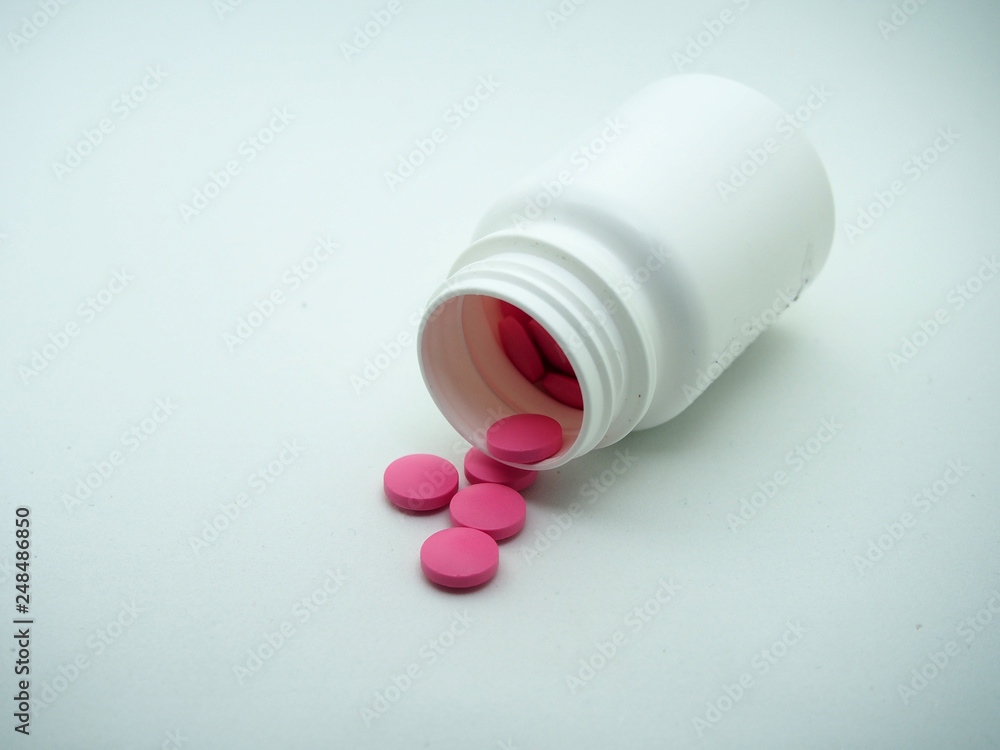 Red tablets are poured from a white plastic jar. Red tablets are poured from a white plastic jar.