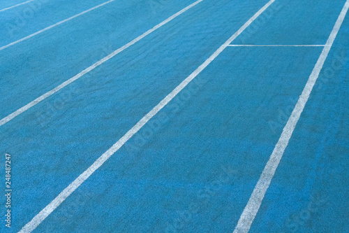 Fragment of blue synthetic surface of running tracks  of athletics stadium with white lines as texture  background  abstract 