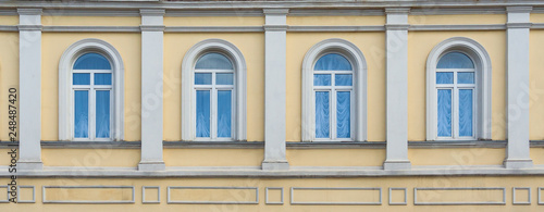 Close up view on a facade of ancient yellow building with four arched windows and white pilasters as texture