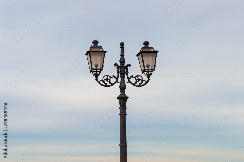 Φωτογραφία An ornate street lamp with double light made of wrought iron, in a beauty sky background