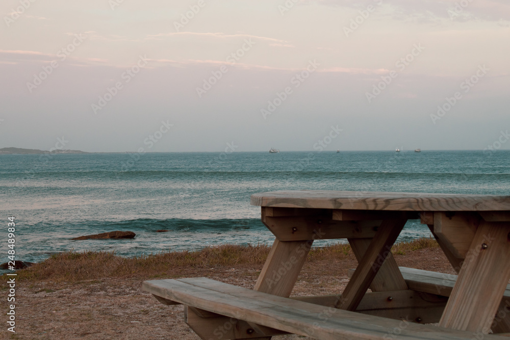 Wooden public pic nic table overlooking the south african ocean; almos astunset, pink light