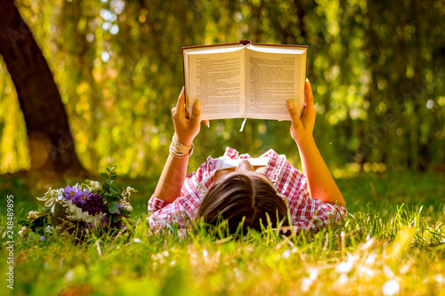 Young woman reading a book in the park with flowers