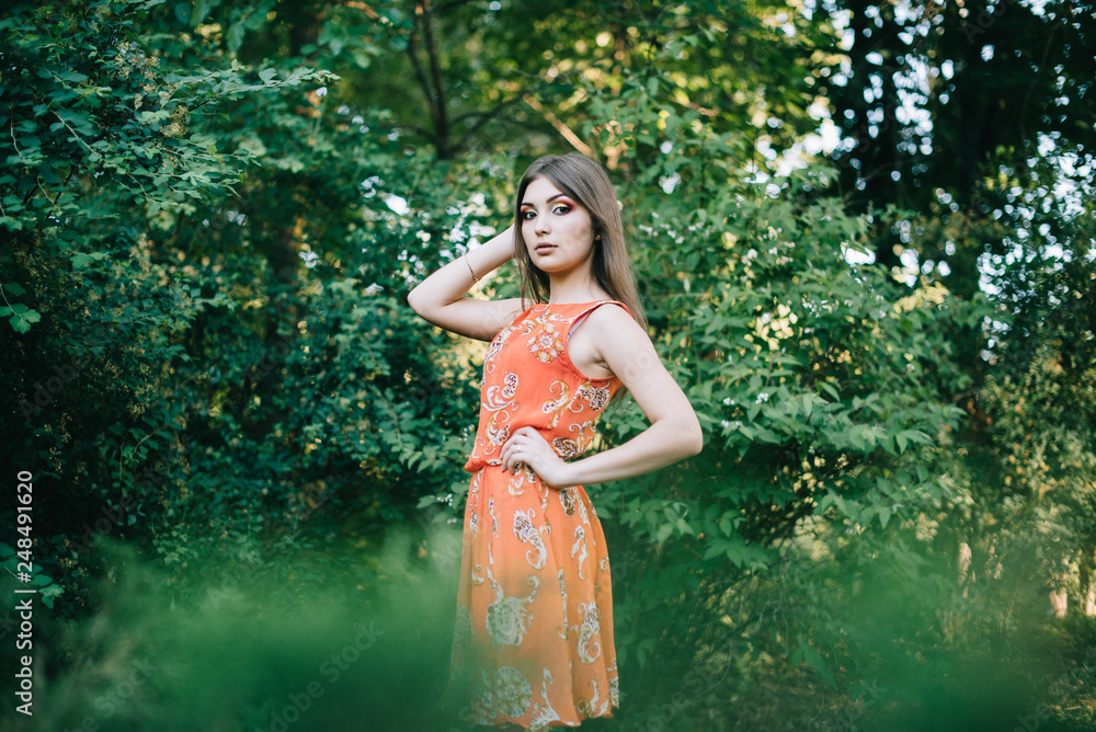 Fototapeta premium Beautiful young girl in a summer red dress in a park