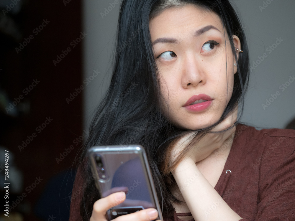 Image of Asian Chinese Thai Filipino beautiful happy young woman looking, using mobile phone at home, checking shopping application, thinking what to buy, promotion sales, online shopping Image of Asian Chinese Thai Filipino beautiful happy young woman looking, using mobile phone at home, checking shopping application, thinking what to buy, promotion sales, online shopping