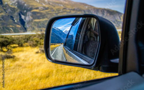 Roadtrip/car traveling concept. View of back car mirror with mountain and road scenery. Aoraki/Mount Cook National Park, South Island of New Zealand.