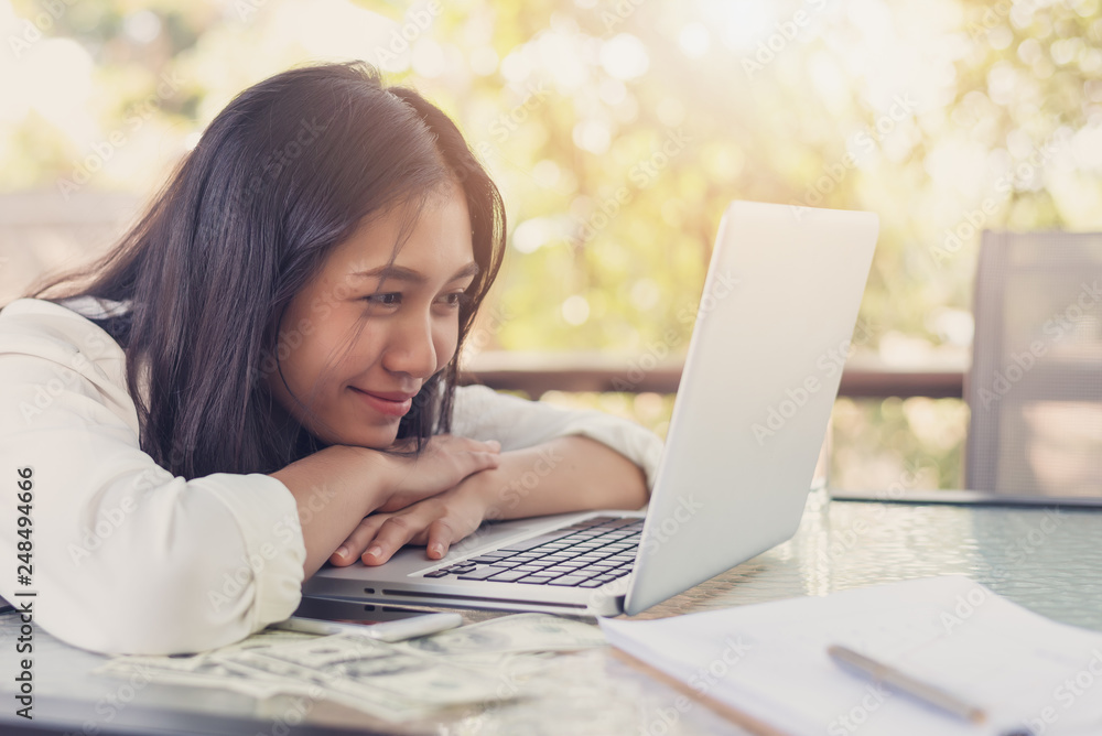 Online worker concept, Asian women smiling and using laptops with the dollar on the desk Online worker concept, Asian women smiling and using laptops with the dollar on the desk
