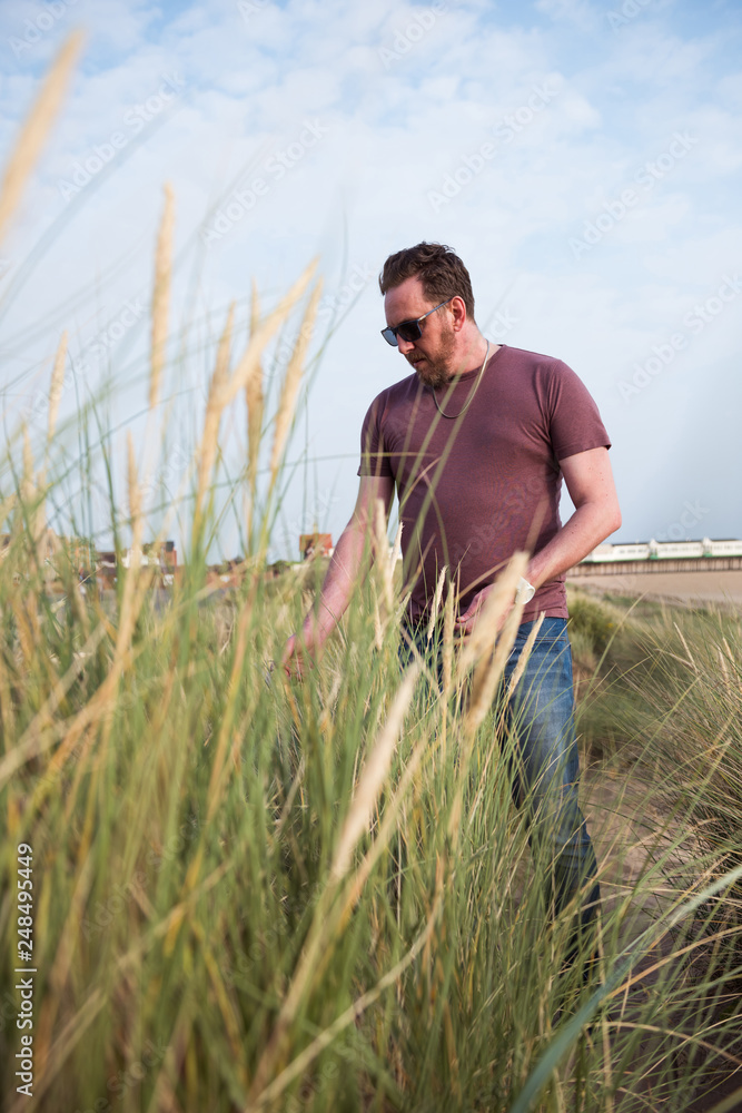 A man on the Beach sand dunes on a beautiful sunny warm evening. Exercise and outdoor walking on sandy golden sand dunes with green  grass reads.