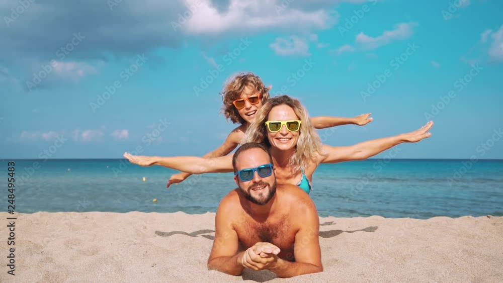 Happy family lying on the beach. People having fun on summer vacation. Father, mother and child against blue sea and sky background. Holiday travel concept Happy family lying on the beach. People having fun on summer vacation. Father, mother and child against blue sea and sky background. Holiday travel concept