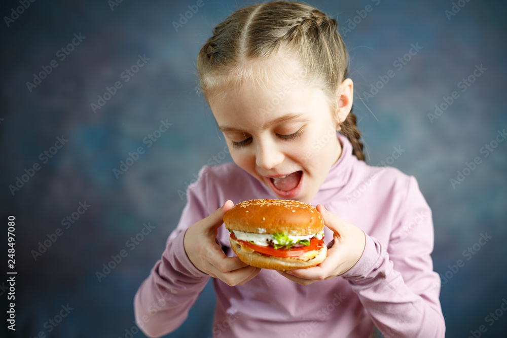 Little cute girl eating a Burger in a cafe, concept of a children's fast food meal Little cute girl eating a Burger in a cafe, concept of a children's fast food meal