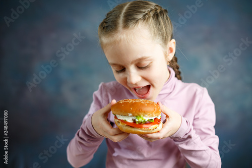 Little cute girl eating a Burger in a cafe, concept of a children's fast food meal