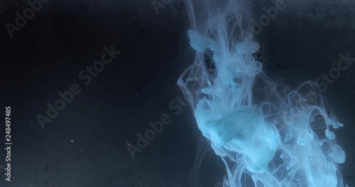 A drop of paint dissolves in water. On black background.