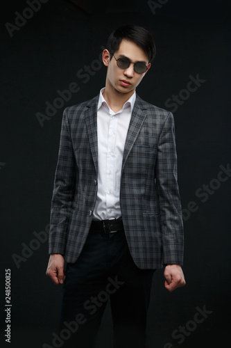 Young asian guy in a suit and sunglasses isolated on dark background.