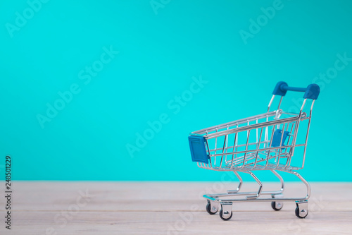 Emtye shopping cart on wooden table with blue background