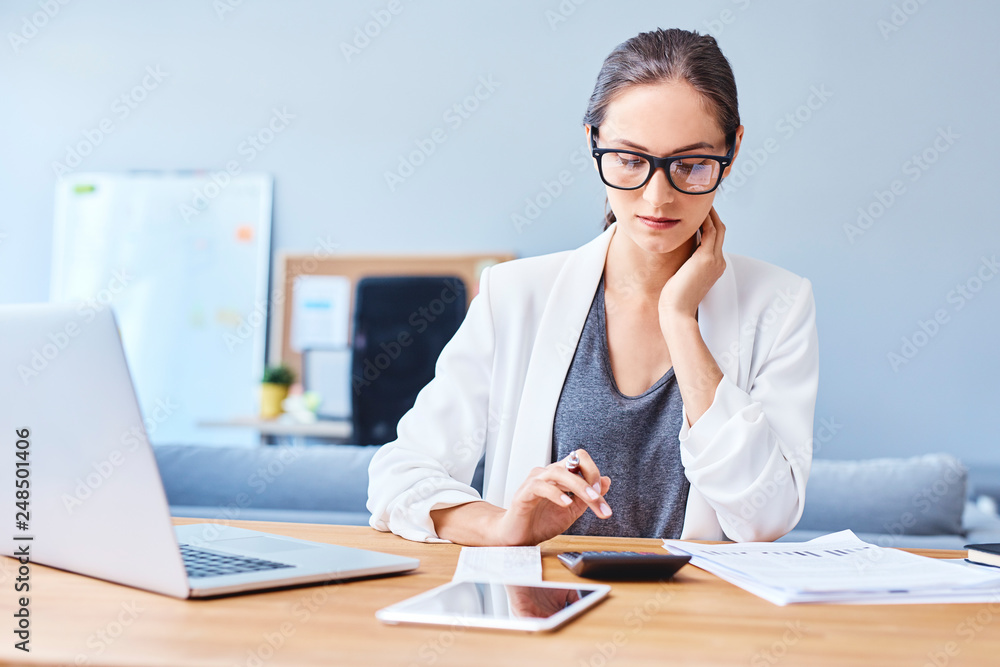 Thoughtful woman managing budget and finances using calculator in office Thoughtful woman managing budget and finances using calculator in office