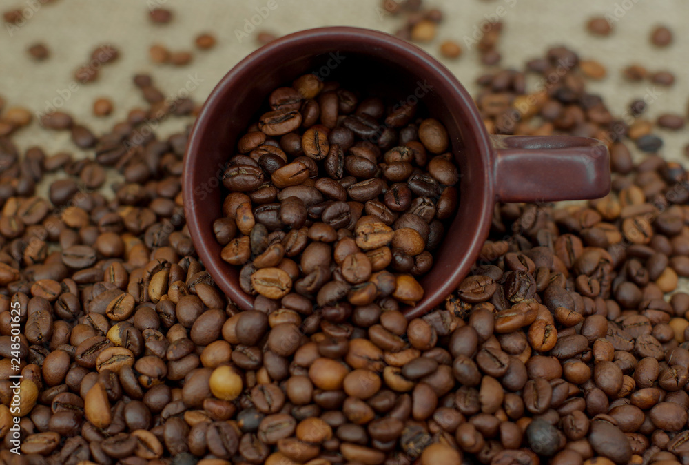 Fototapeta premium A cup of coffee full of coffee beans. Coffee cup and coffee beans. Grain coffee on burlap.